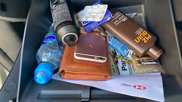 Photo of items in a glovebox including a phone, aerosol, water, batteries
