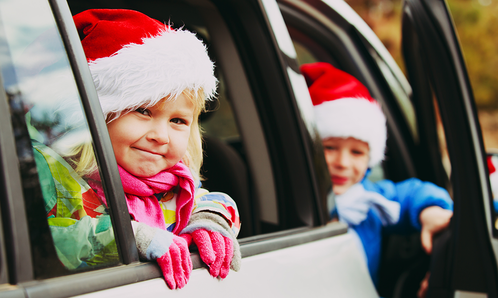 Two children smiling leaning out of car windows in Santa hats and winter clothes