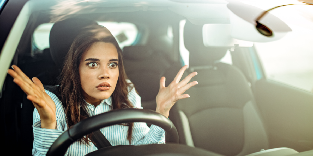 Woman in car with a frustrated expression and her hands raised in anger