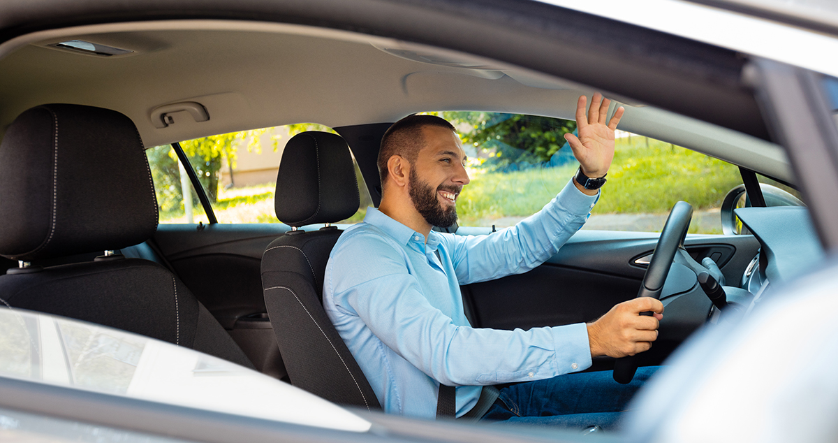 Young man happily driving a car and waving - being courteous