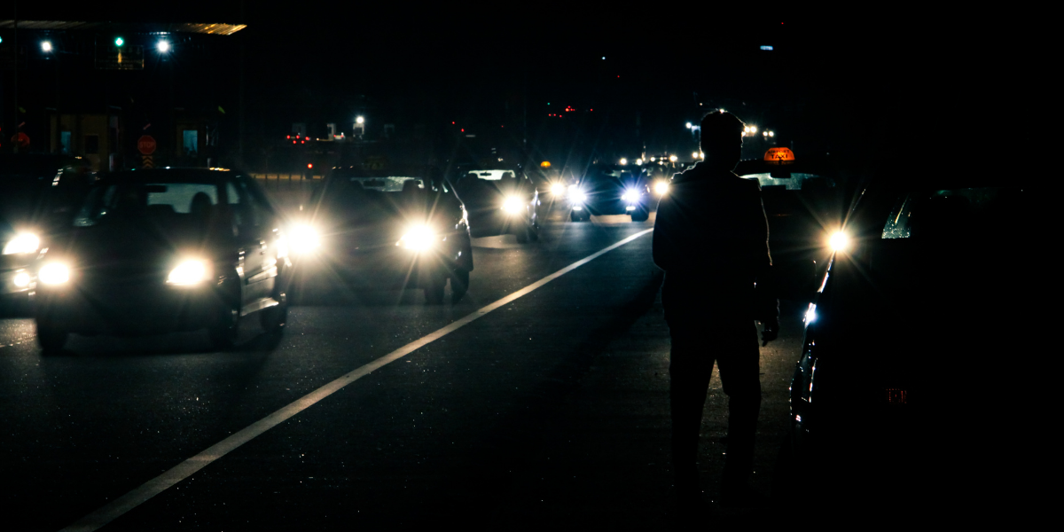 Queue of cars with headlights on in the darkness and a driver stood next to his car